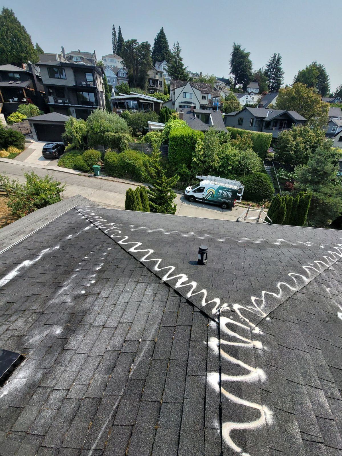 Composition roof in Laurelhurst with a wavy white line of moss-prevention treatment running along the ridge and hip, a Renova van and ladder on the street below, and neighboring homes on the slope behind